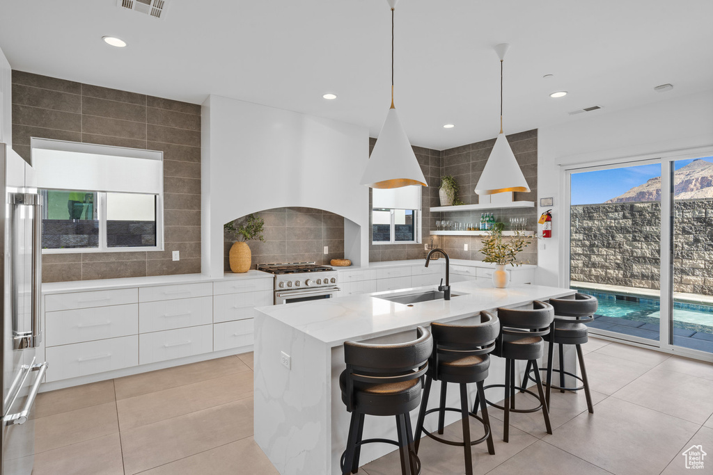 Kitchen with an island with sink, hanging light fixtures, sink, white cabinetry, and stainless steel appliances