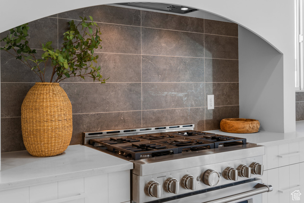 Details with backsplash, gas range, and white cabinetry