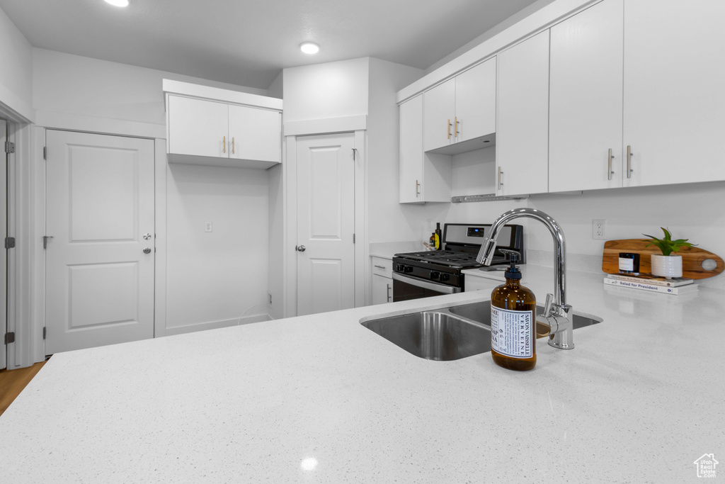 Kitchen with stainless steel range with gas stovetop, white cabinetry, and sink