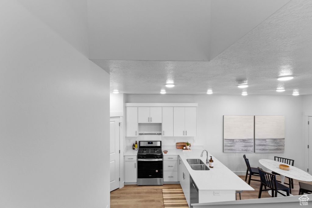 Kitchen with light wood-type flooring, stainless steel range oven, sink, white cabinets, and a textured ceiling