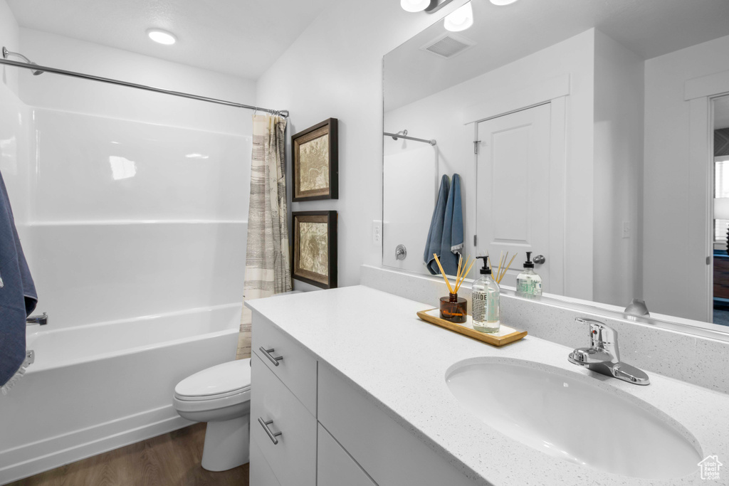 Full bathroom featuring hardwood / wood-style flooring, vanity, shower / bath combo with shower curtain, and toilet