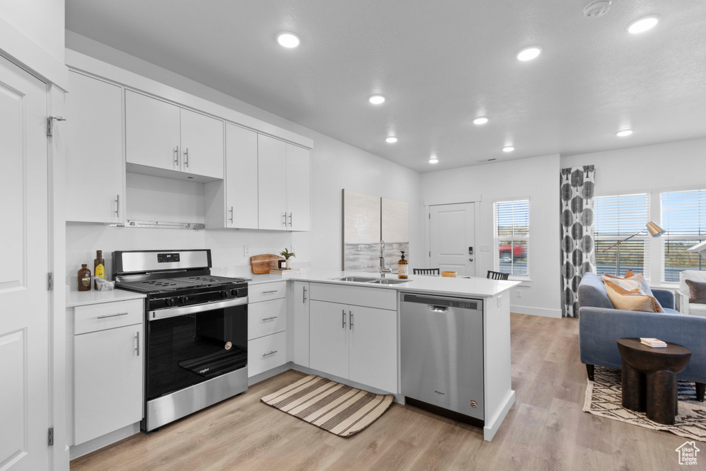 Kitchen with white cabinets, sink, light hardwood / wood-style floors, kitchen peninsula, and appliances with stainless steel finishes