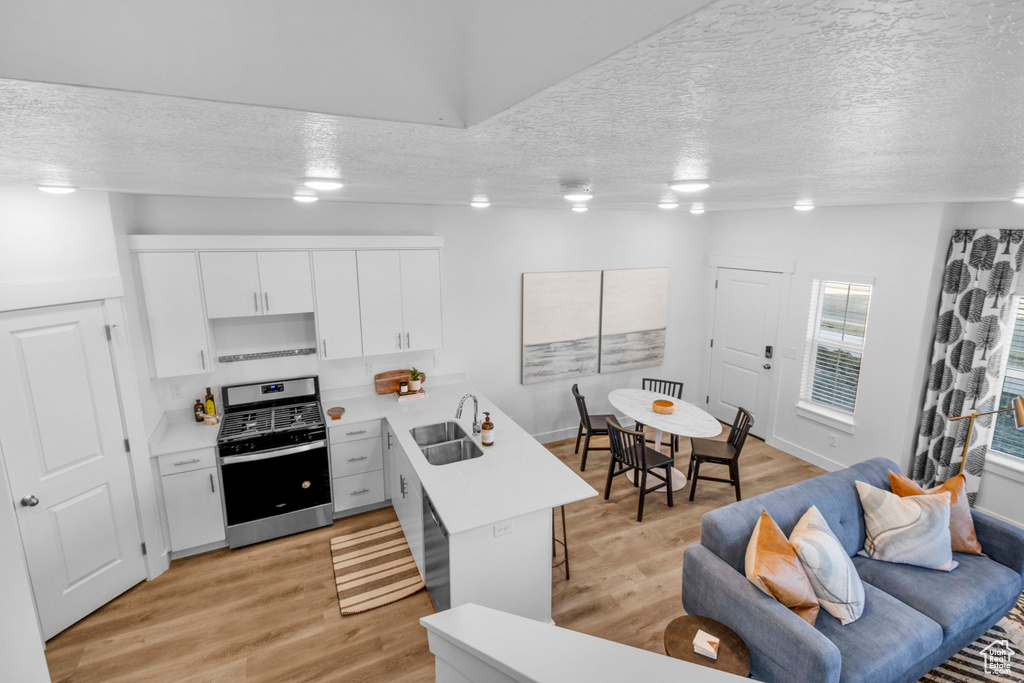 Kitchen with light hardwood / wood-style floors, white cabinets, stainless steel range oven, and sink