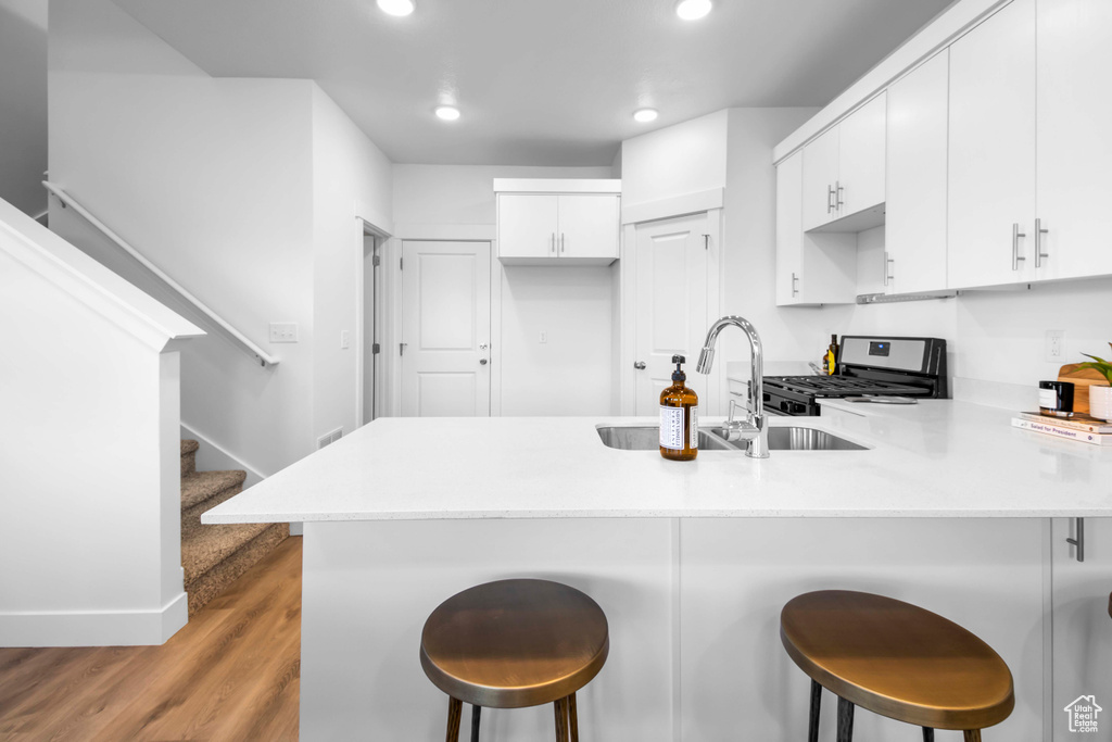 Kitchen with light hardwood / wood-style floors, a breakfast bar area, range with gas cooktop, kitchen peninsula, and white cabinetry