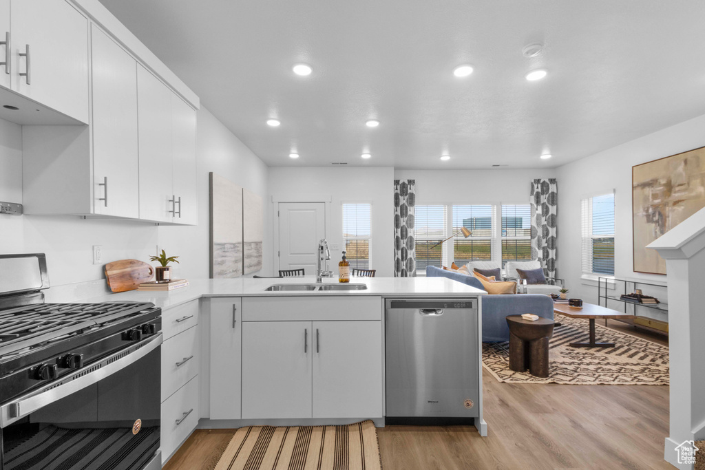 Kitchen with light wood-type flooring, sink, stainless steel appliances, kitchen peninsula, and white cabinetry