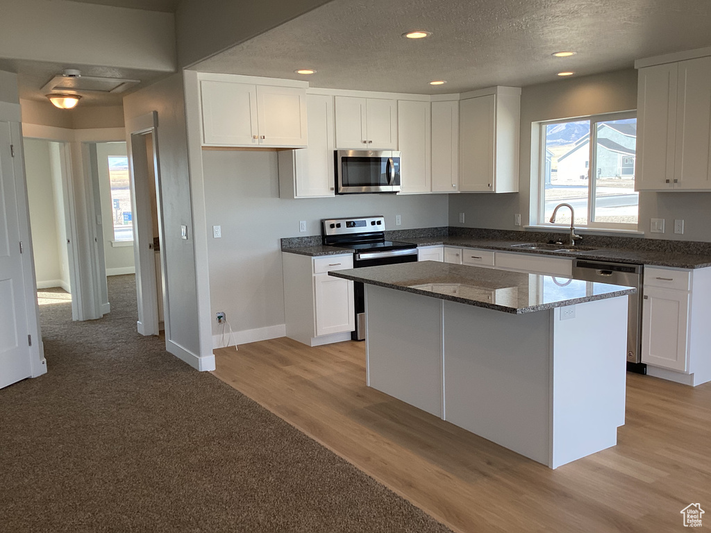 Kitchen with light hardwood / wood-style flooring, sink, stainless steel appliances, a center island, and white cabinetry