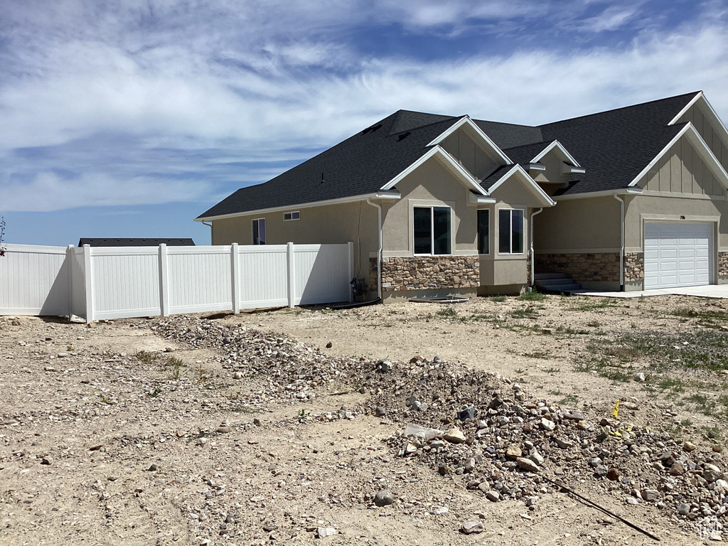 View of side of property with stone siding, an attached garage, board and batten siding, and dirt driveway