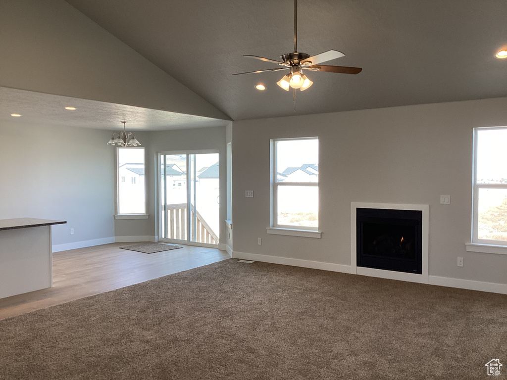 Unfurnished living room with ceiling fan with notable chandelier, high vaulted ceiling, and light hardwood / wood-style flooring
