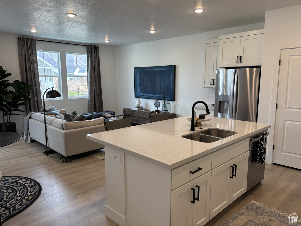 Kitchen featuring light wood-type flooring, sink, an island with sink, appliances with stainless steel finishes, and white cabinetry