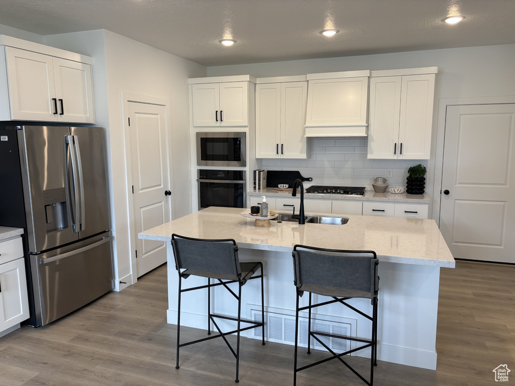 Kitchen with a kitchen island with sink, stainless steel appliances, hardwood / wood-style floors, and white cabinetry