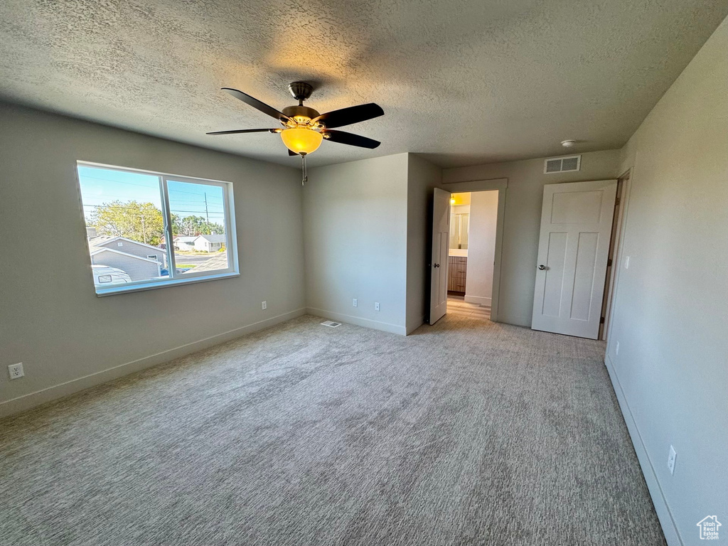 Unfurnished bedroom with ensuite bathroom, light colored carpet, ceiling fan, and a textured ceiling