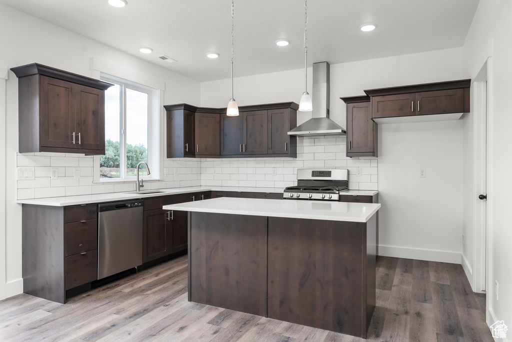 Kitchen featuring wall chimney exhaust hood, wood-type flooring, gas stove, dishwasher, and hanging light fixtures