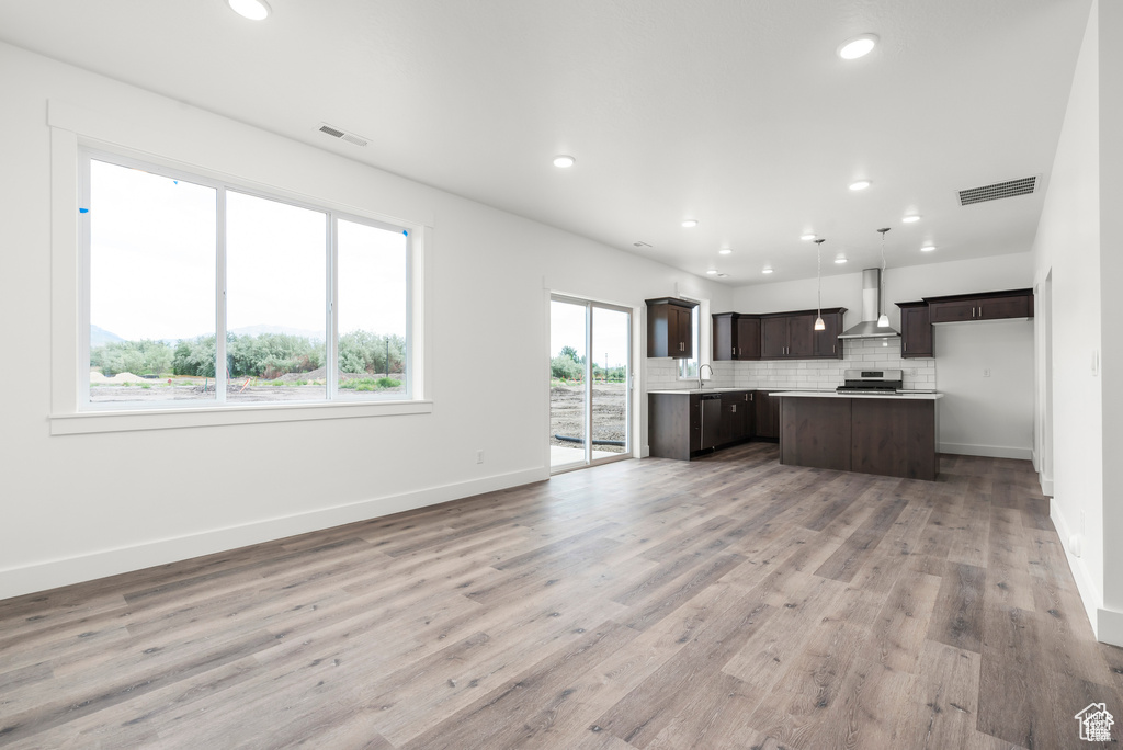 Kitchen with wall chimney range hood, stainless steel range, a kitchen island, decorative light fixtures, and hardwood / wood-style flooring