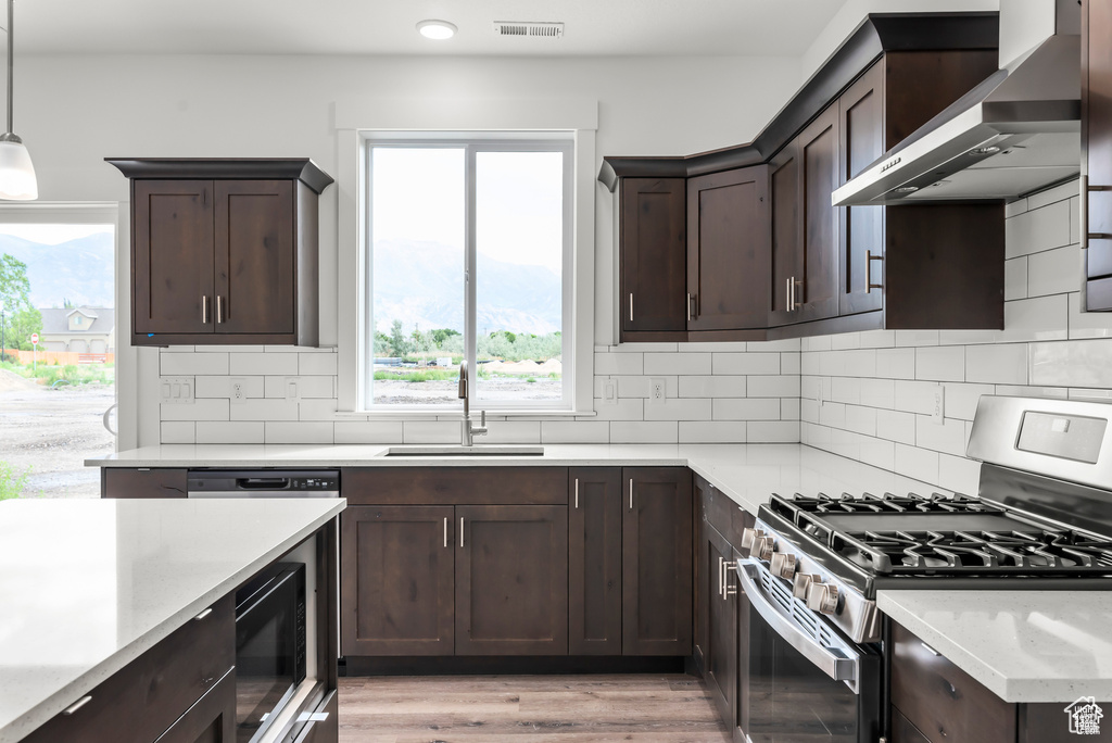 Kitchen featuring wall chimney range hood, stainless steel gas range oven, pendant lighting, light hardwood / wood-style flooring, and sink