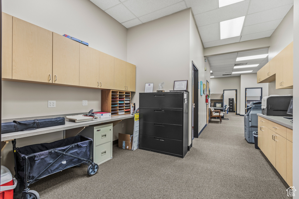 Office space with a drop ceiling, built in desk, and light carpet