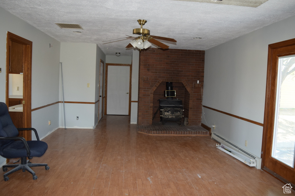 Unfurnished living room featuring a wood stove, hardwood / wood-style flooring, a textured ceiling, and a baseboard radiator