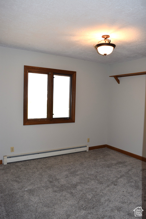 Carpeted empty room featuring a baseboard radiator and a textured ceiling