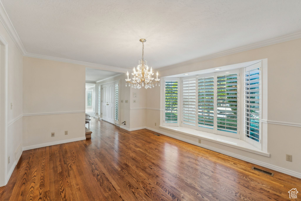 Empty room featuring ornamental molding, an inviting chandelier, and dark hardwood / wood-style floors