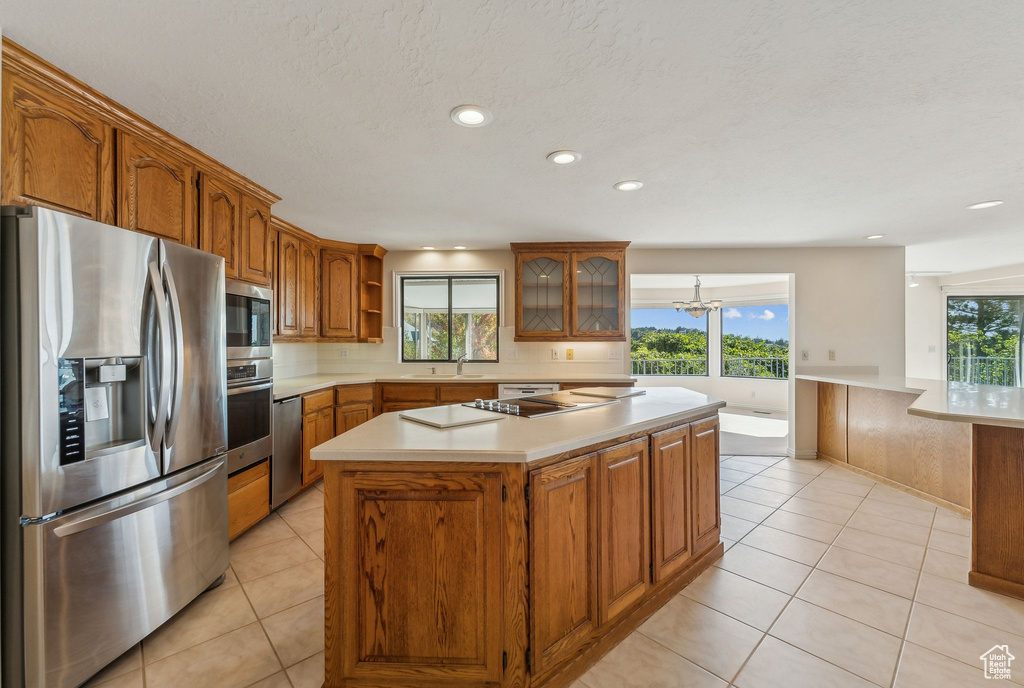 Kitchen with a kitchen island, stainless steel appliances, sink, light tile patterned flooring, and a textured ceiling