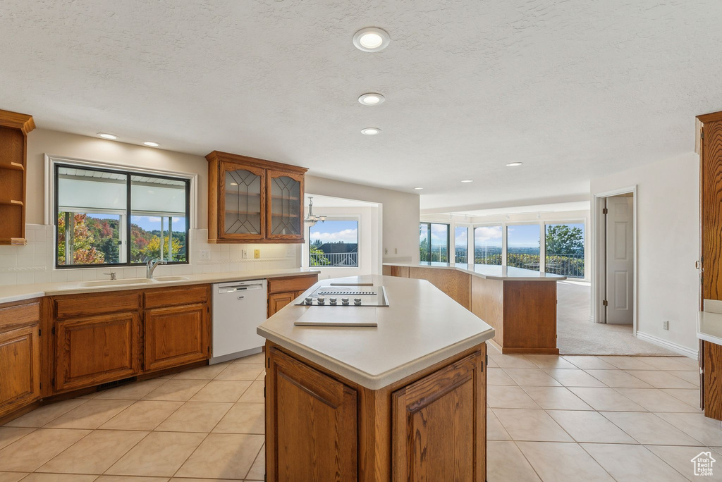 Kitchen featuring light tile patterned flooring, sink, dishwasher, backsplash, and a center island