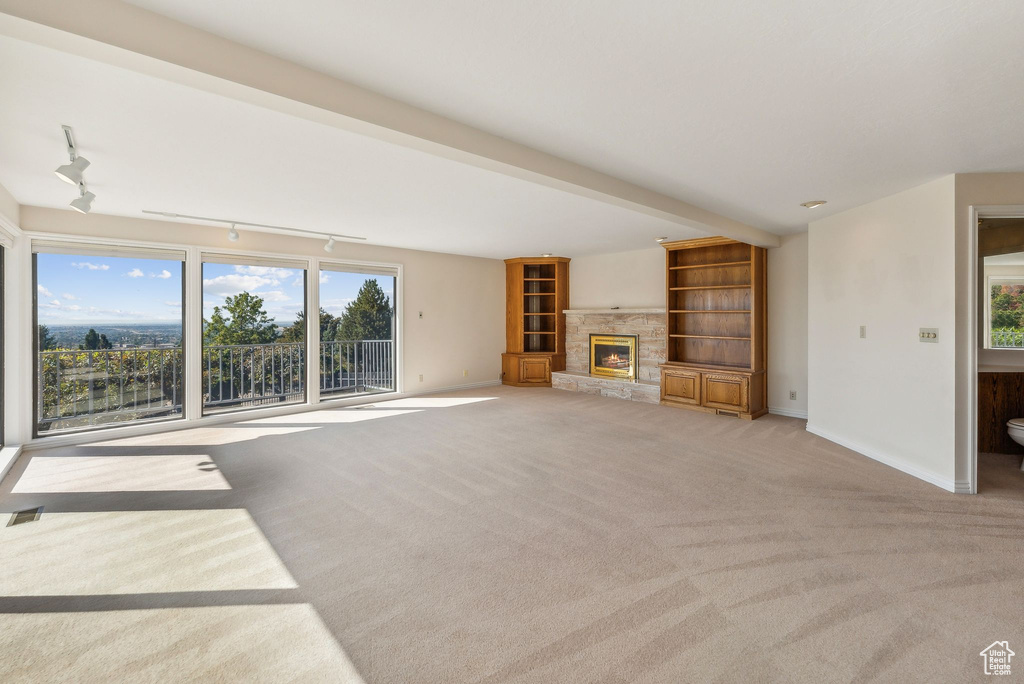 Unfurnished living room with light carpet, plenty of natural light, a stone fireplace, and rail lighting