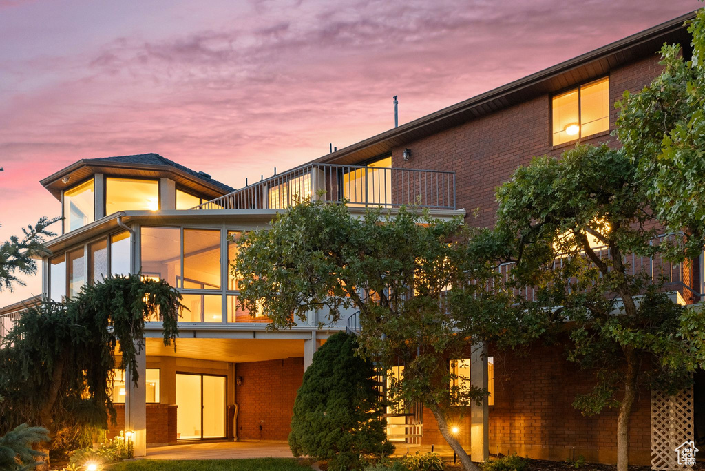 Back house at dusk with a sunroom and a balcony