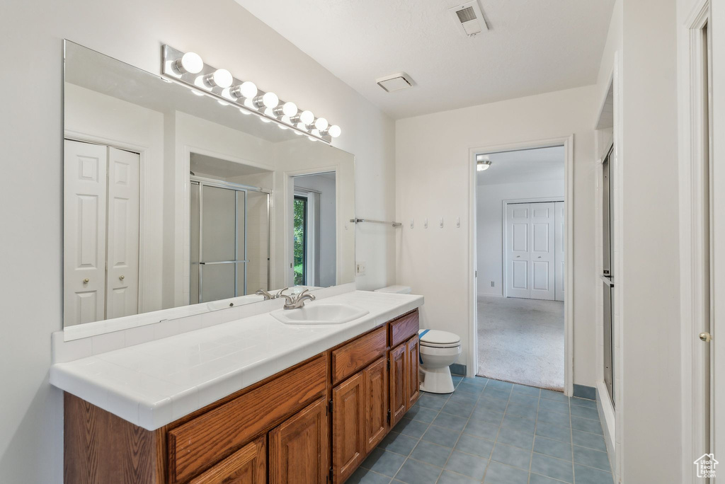 Bathroom with walk in shower, tile patterned floors, vanity, and toilet