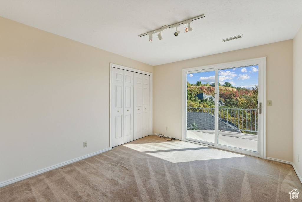 Unfurnished bedroom featuring access to exterior, light carpet, a closet, and rail lighting