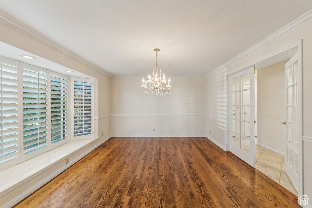 Unfurnished dining area featuring ornamental molding, hardwood / wood-style floors, and a notable chandelier