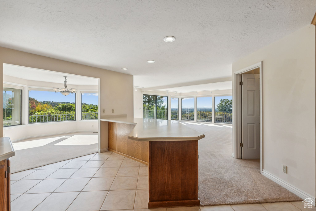 Kitchen with a chandelier, decorative light fixtures, kitchen peninsula, light tile patterned floors, and a textured ceiling