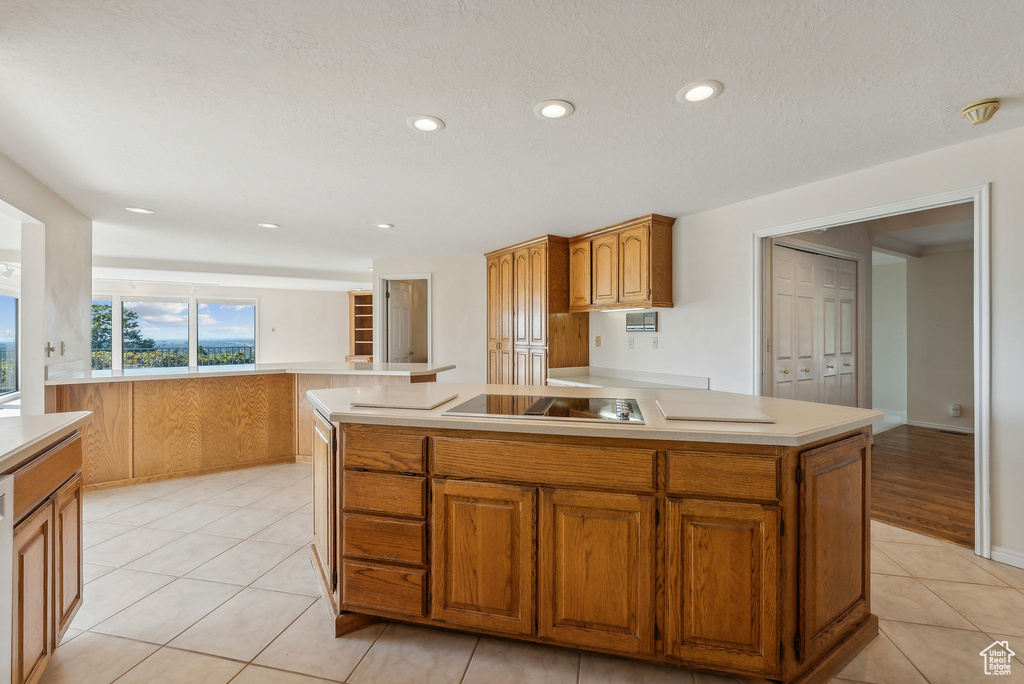 Kitchen with light tile patterned flooring, a kitchen island with sink, a textured ceiling, and black electric stovetop