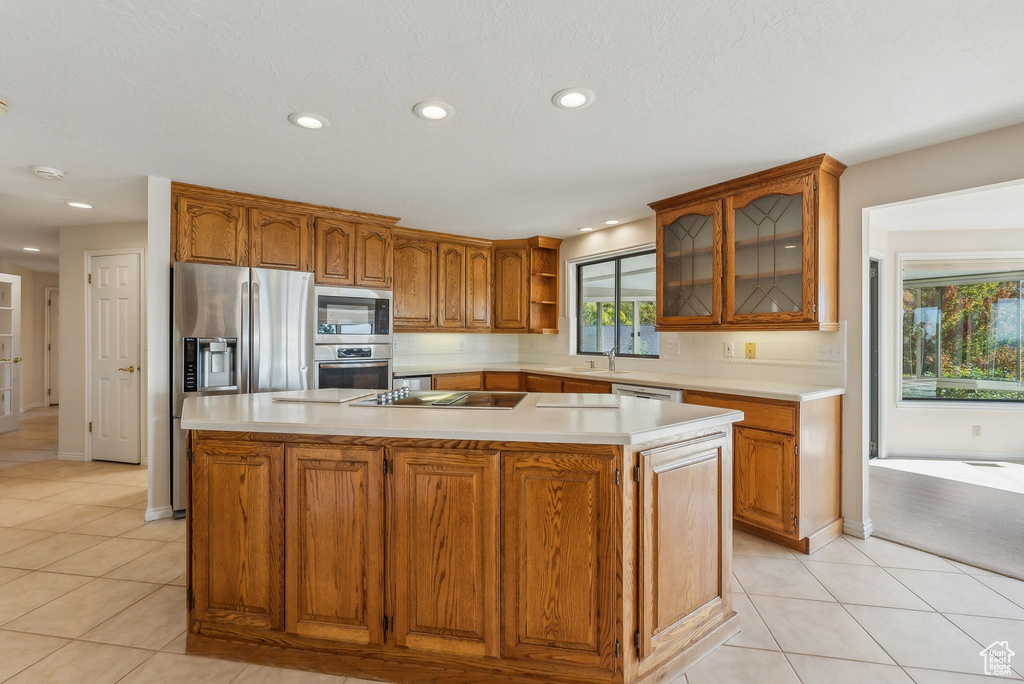 Kitchen featuring appliances with stainless steel finishes, a textured ceiling, light tile patterned floors, and an island with sink