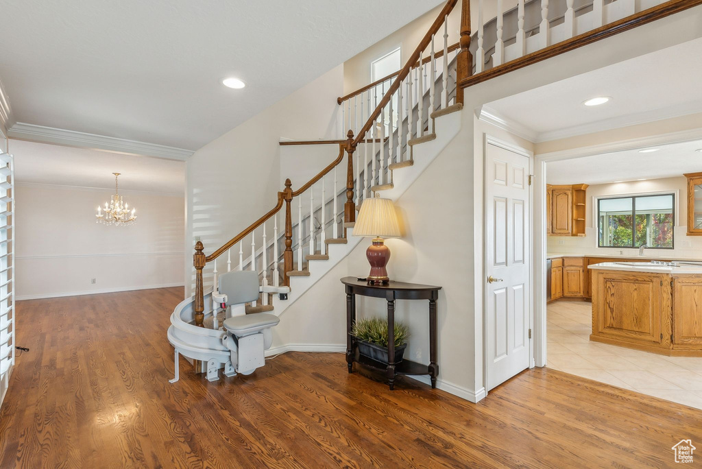 Stairway with hardwood / wood-style flooring, crown molding, a notable chandelier, and sink