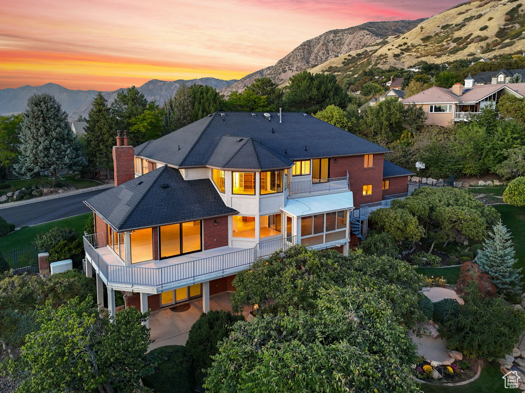 Back house at dusk with a carport, a balcony, a mountain view, and a sunroom