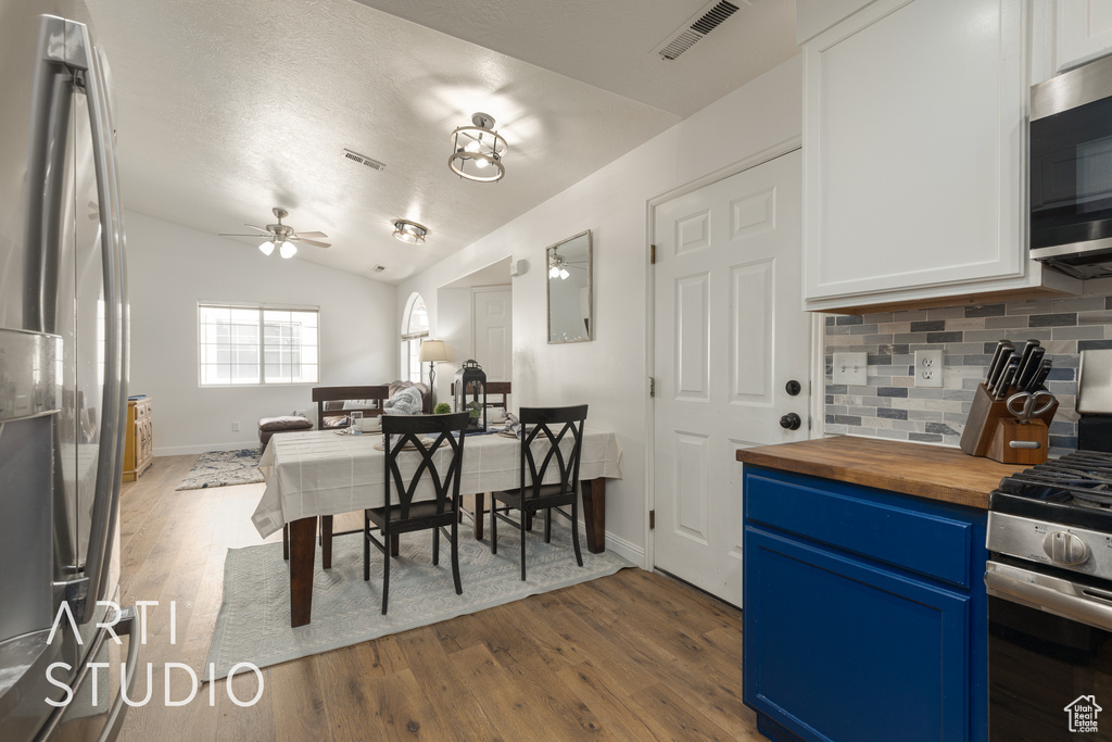 Kitchen with blue cabinets, hardwood / wood-style floors, wood counters, stainless steel appliances, and lofted ceiling