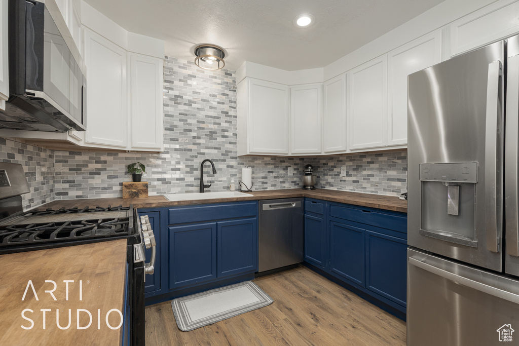 Kitchen featuring white cabinets, sink, blue cabinetry, stainless steel appliances, and butcher block counters