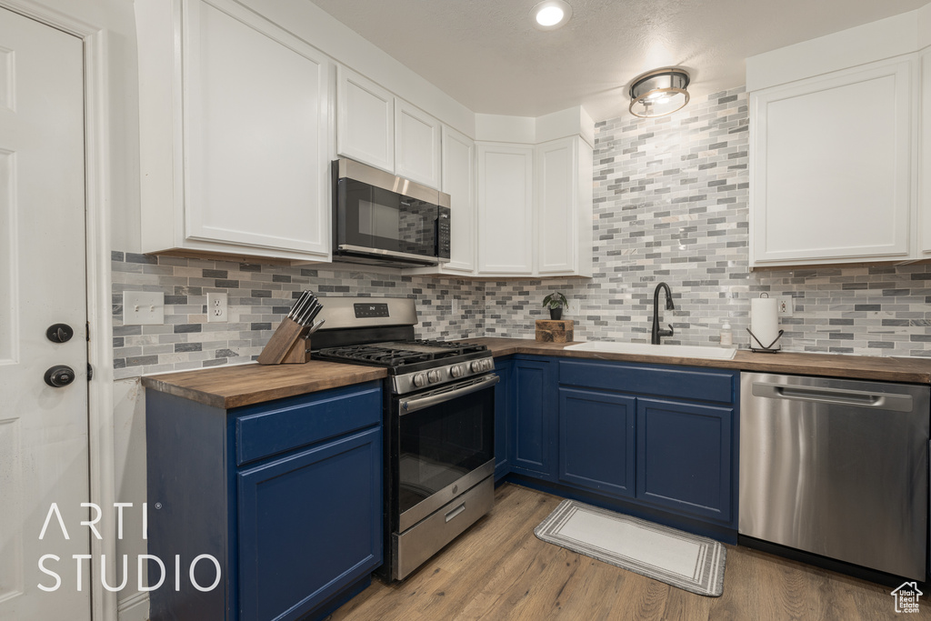 Kitchen with appliances with stainless steel finishes, wood counters, sink, and blue cabinetry