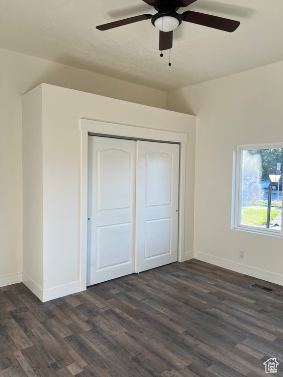 Unfurnished bedroom with ceiling fan, a closet, and dark wood-type flooring