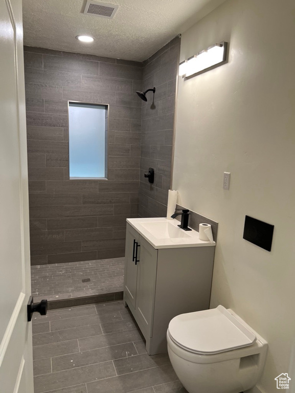 Bathroom featuring a textured ceiling, tiled shower, vanity, and toilet