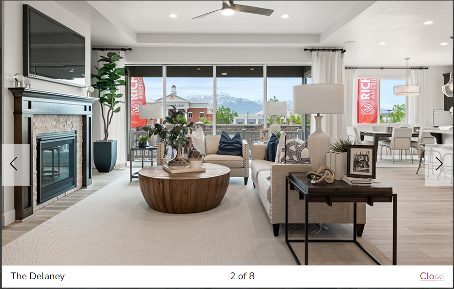 Living room featuring a mountain view, ceiling fan, light wood-type flooring, a tray ceiling, and a stone fireplace