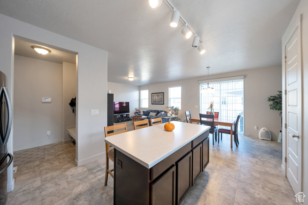 Kitchen with rail lighting, stainless steel fridge, dark brown cabinets, hanging light fixtures, and a center island