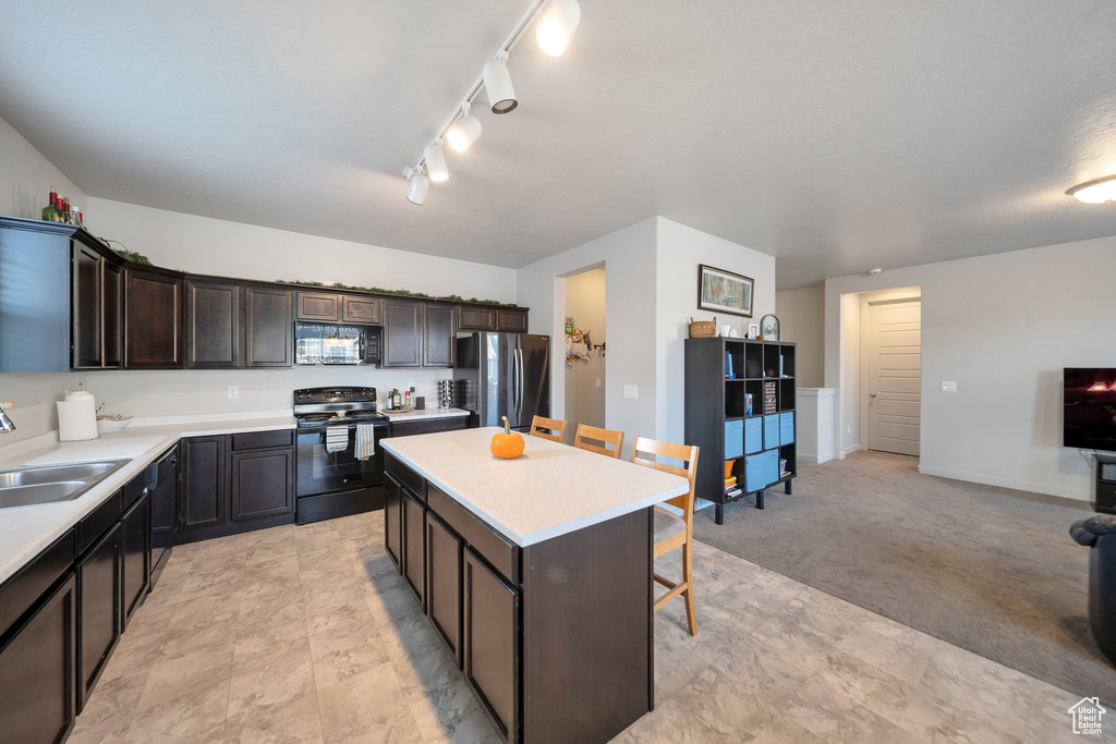 Kitchen featuring a kitchen island, dark brown cabinets, light carpet, sink, and black appliances