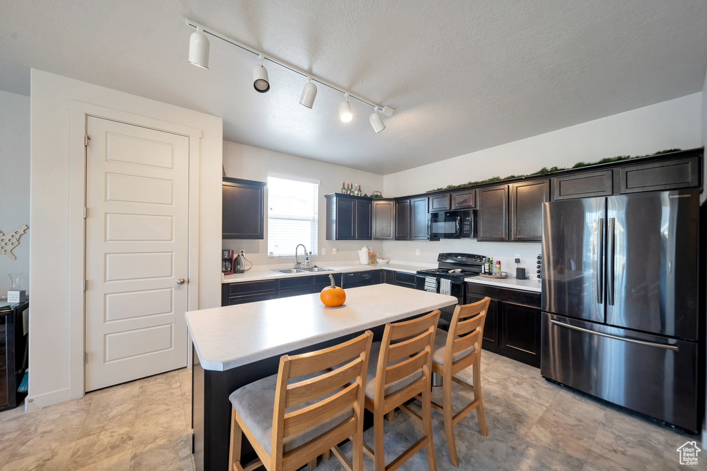 Kitchen featuring sink, a kitchen island, rail lighting, black appliances, and a breakfast bar area