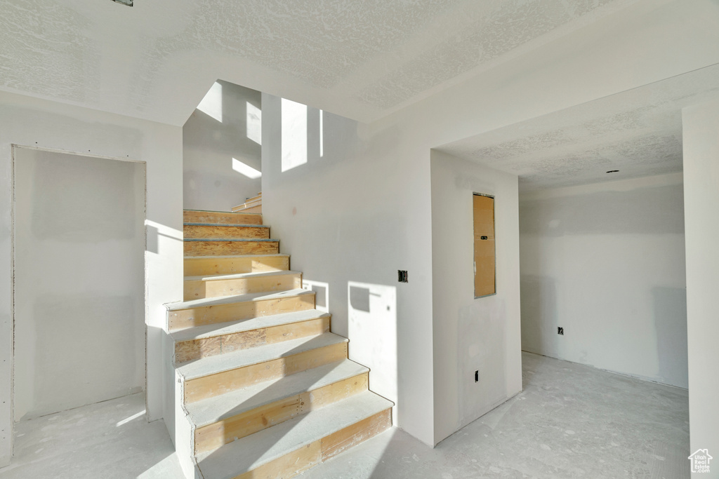 Stairs with a textured ceiling and concrete flooring