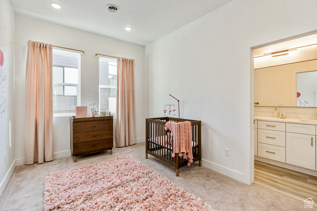 Bedroom with a crib, ensuite bathroom, sink, and light colored carpet