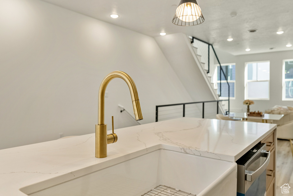 Kitchen featuring light stone counters, decorative light fixtures, sink, and light wood-type flooring