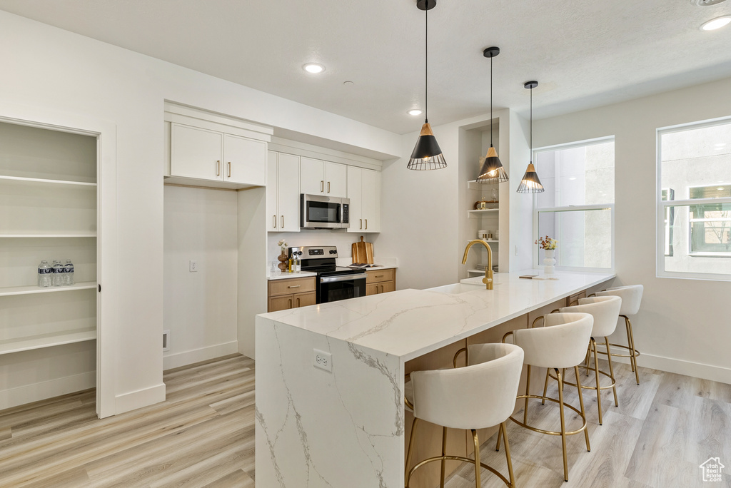 Kitchen with decorative light fixtures, white cabinetry, kitchen peninsula, stainless steel appliances, and light stone countertops