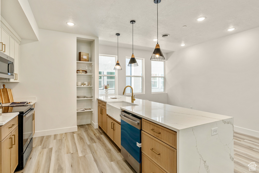 Kitchen with appliances with stainless steel finishes, light brown cabinetry, decorative light fixtures, light stone countertops, and light hardwood / wood-style flooring