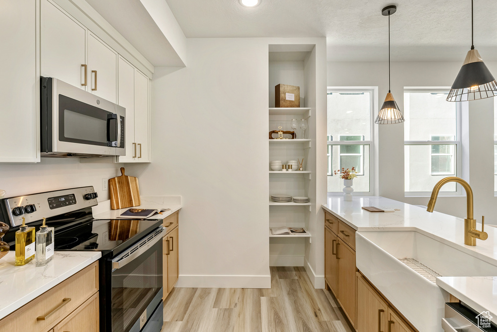 Kitchen featuring appliances with stainless steel finishes, pendant lighting, white cabinetry, sink, and light hardwood / wood-style floors