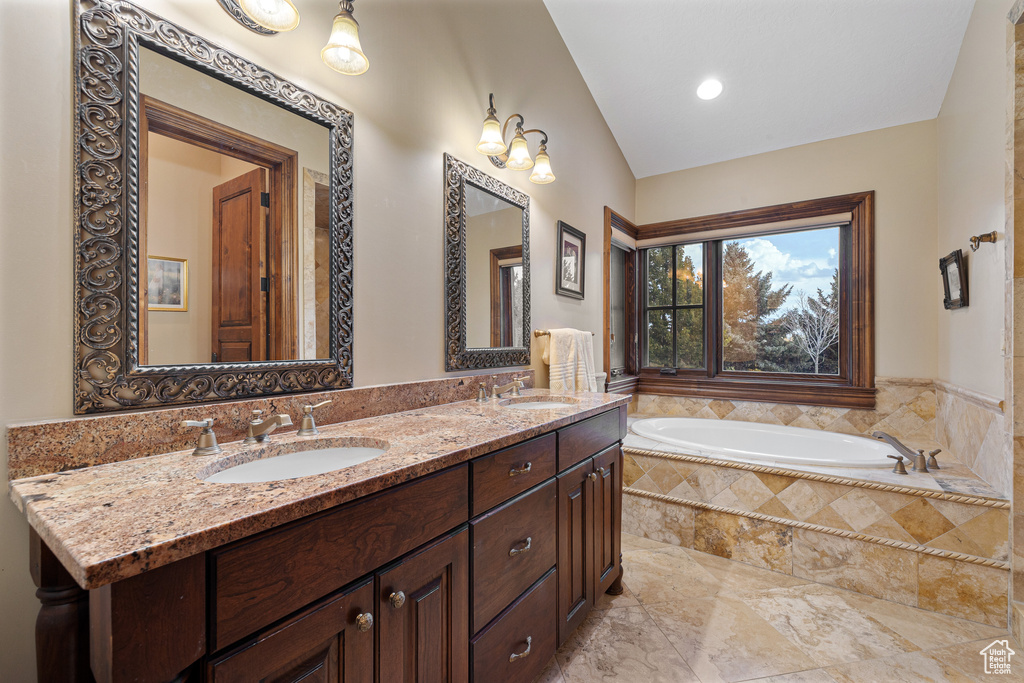 Bathroom with lofted ceiling, a relaxing tiled tub, and vanity